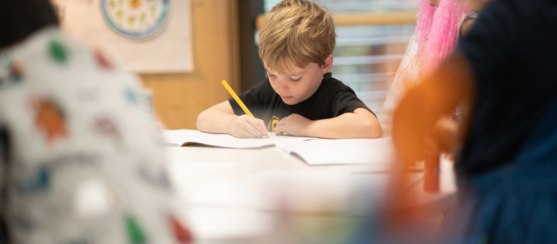little boy writing in a notebook in a classroom